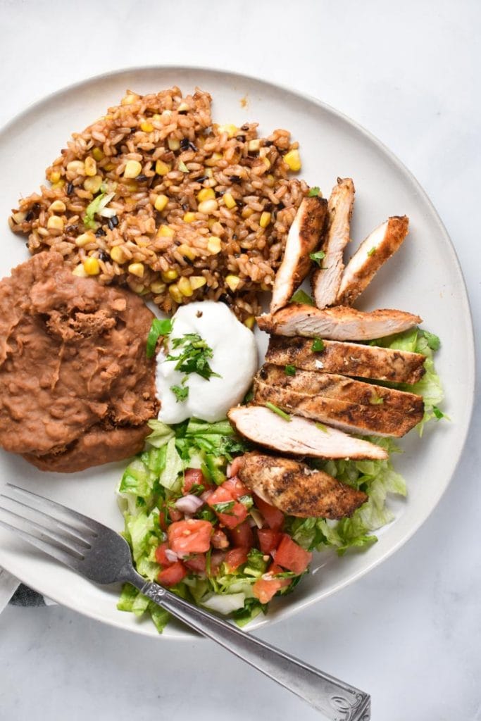 Mexican grilled chicken on a plate with beans, rice, lettuce, tomatoes, and cilantro