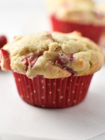 A strawberry cream cheese muffin a red polka dot cup on a white table.