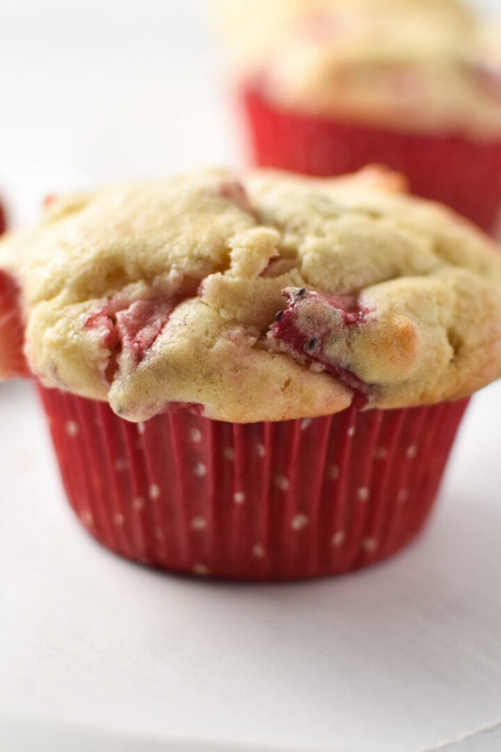 A strawberry cream cheese muffin a red polka dot cup on a white table.