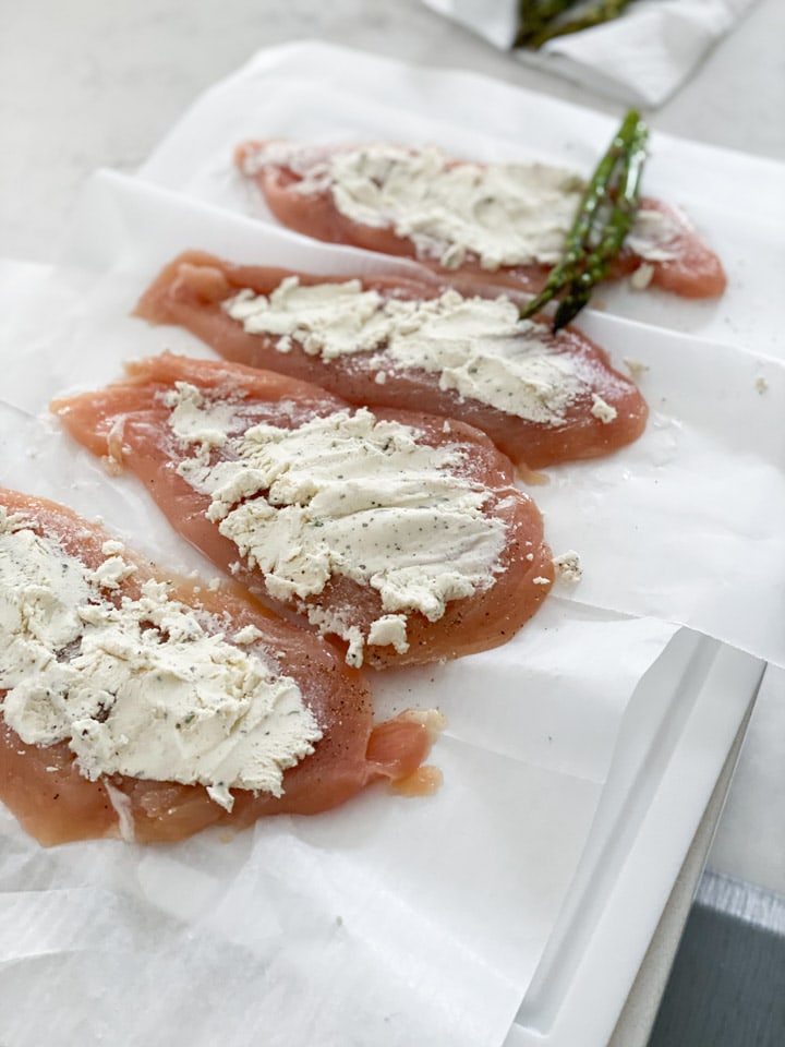 Boursin cheese spread on raw chicken breasts lined up in a row