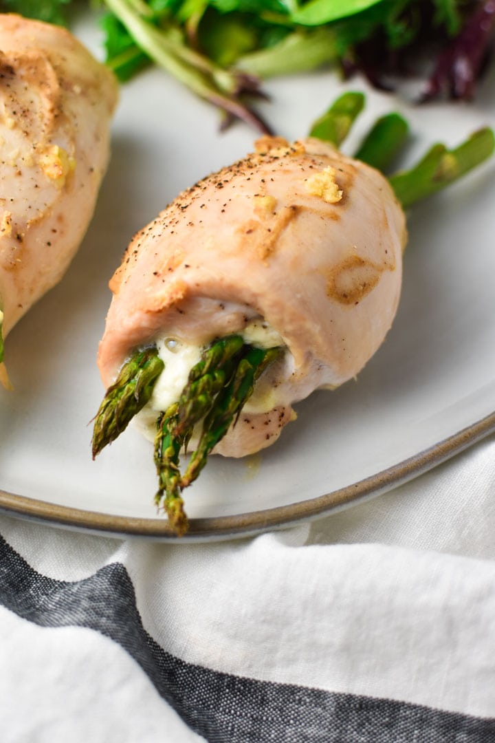 A thin chicken breast that's rolled with Boursin cheese and asparagus next to a side salad