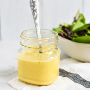 A yellow curry dressing in a mason jar with a spoon