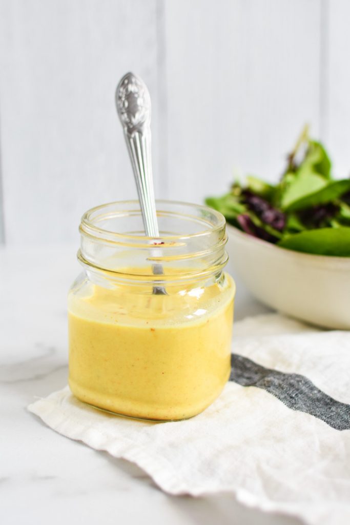 A yellow curry dressing in a mason jar with a spoon