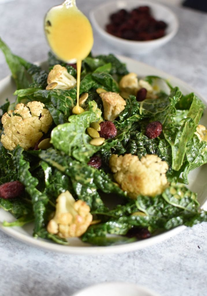 A creamy curry dressing being poured over a kale salad