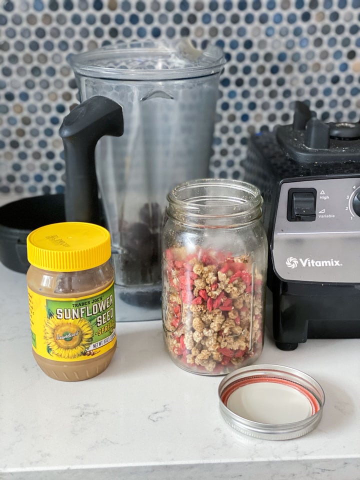 Ingredients for a cherry vanilla smoothie like sunbutter and mulberries next to a blender