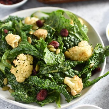 A bowl of kale cauliflower salad next to seeds and a baking sheet
