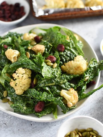 A bowl of kale cauliflower salad next to seeds and a baking sheet