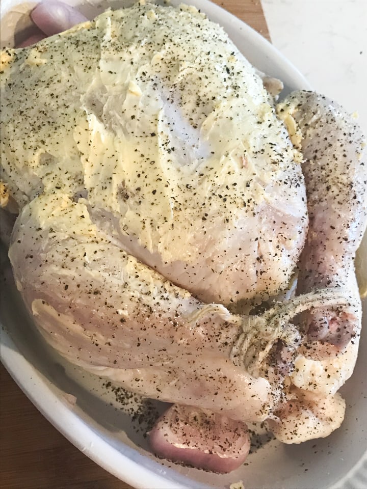 Raw whole chicken covered in butter and pepper