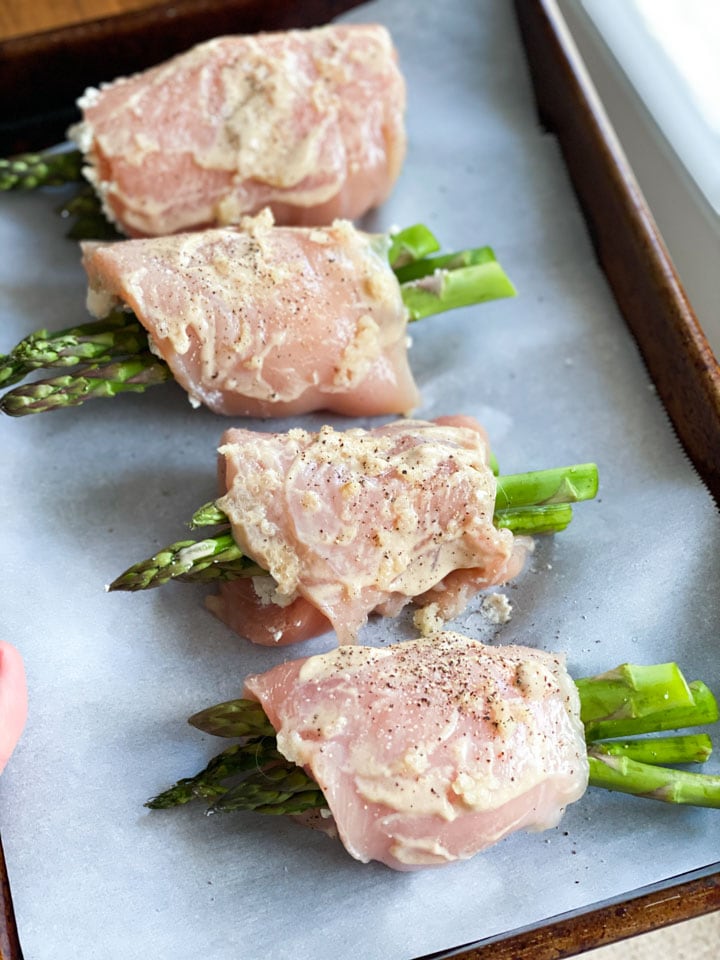 A line of uncooked asparagus stuffed chicken breasts on a baking sheet