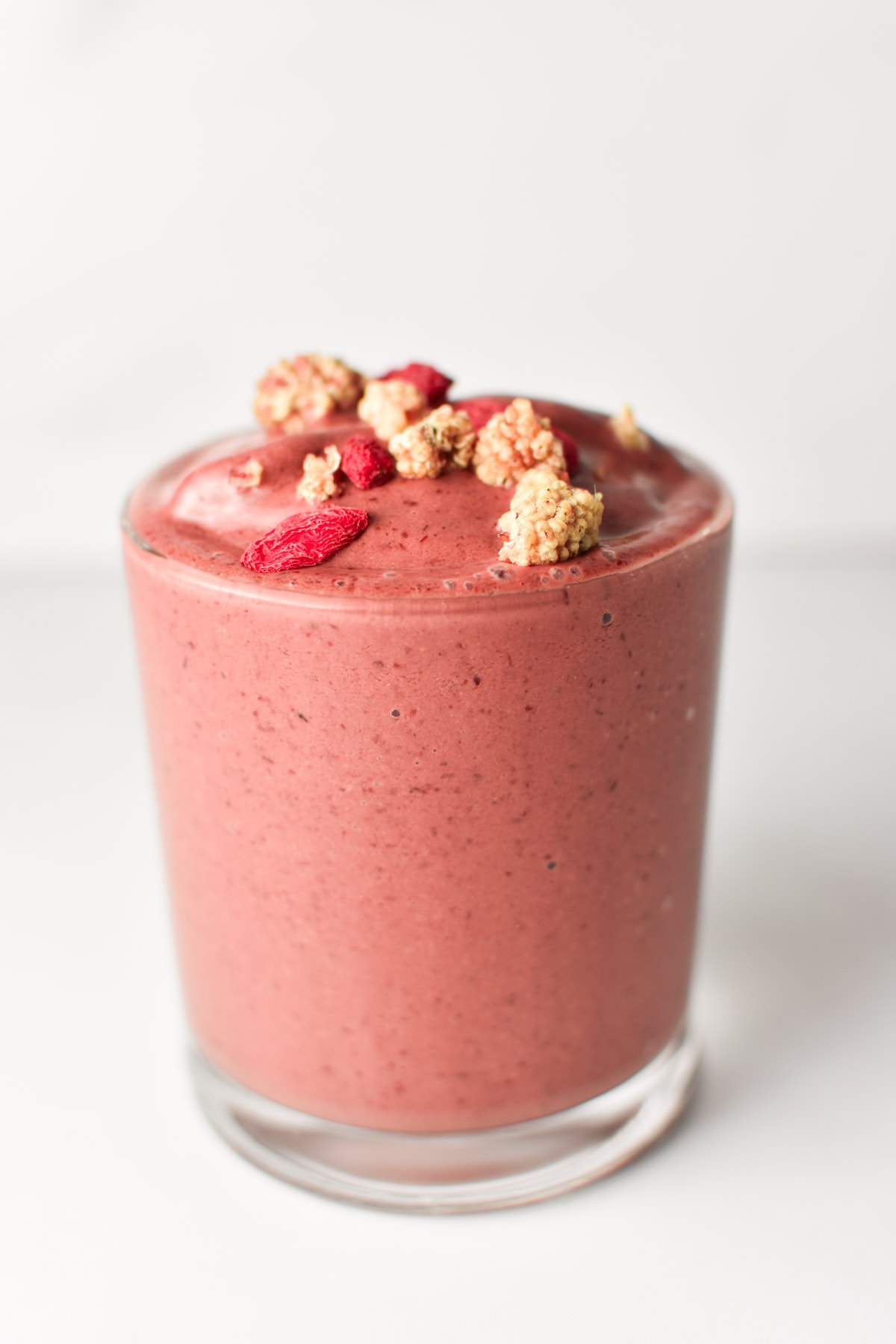 A cherry smoothie in a glass topped with mulberries.