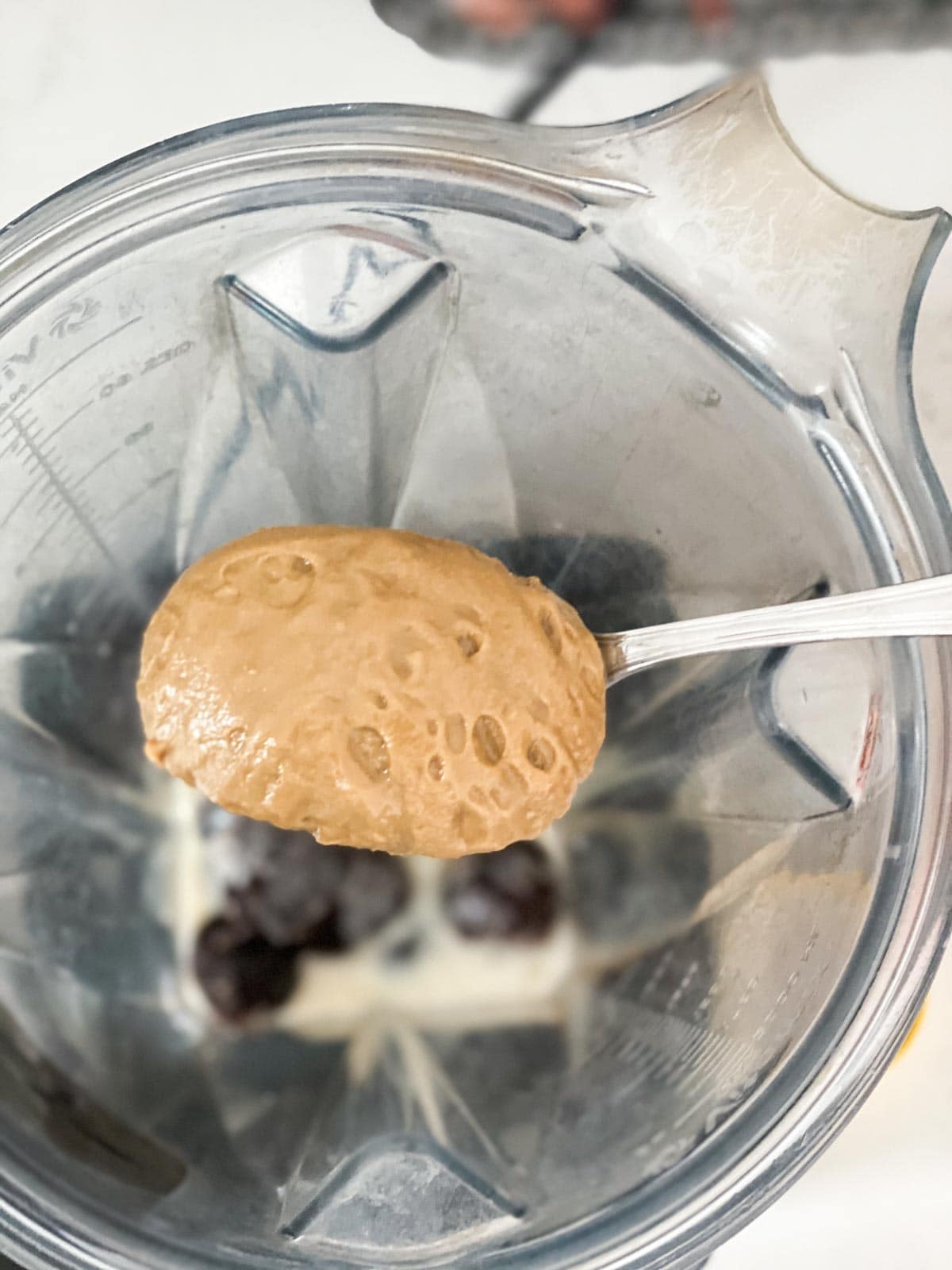 A scoop of sunbutter being put into a blender.