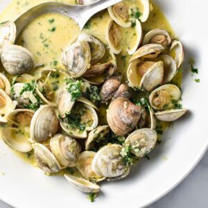 Clams in creamy sauce with parsley in a large white bowl.