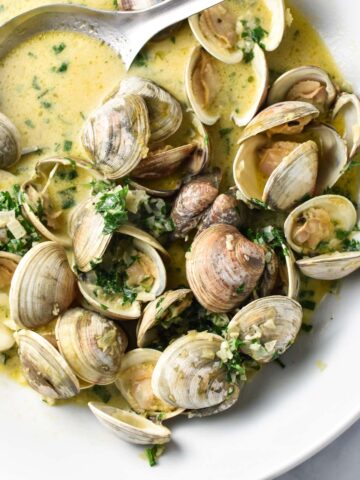 Clams in creamy sauce with parsley in a large white bowl.