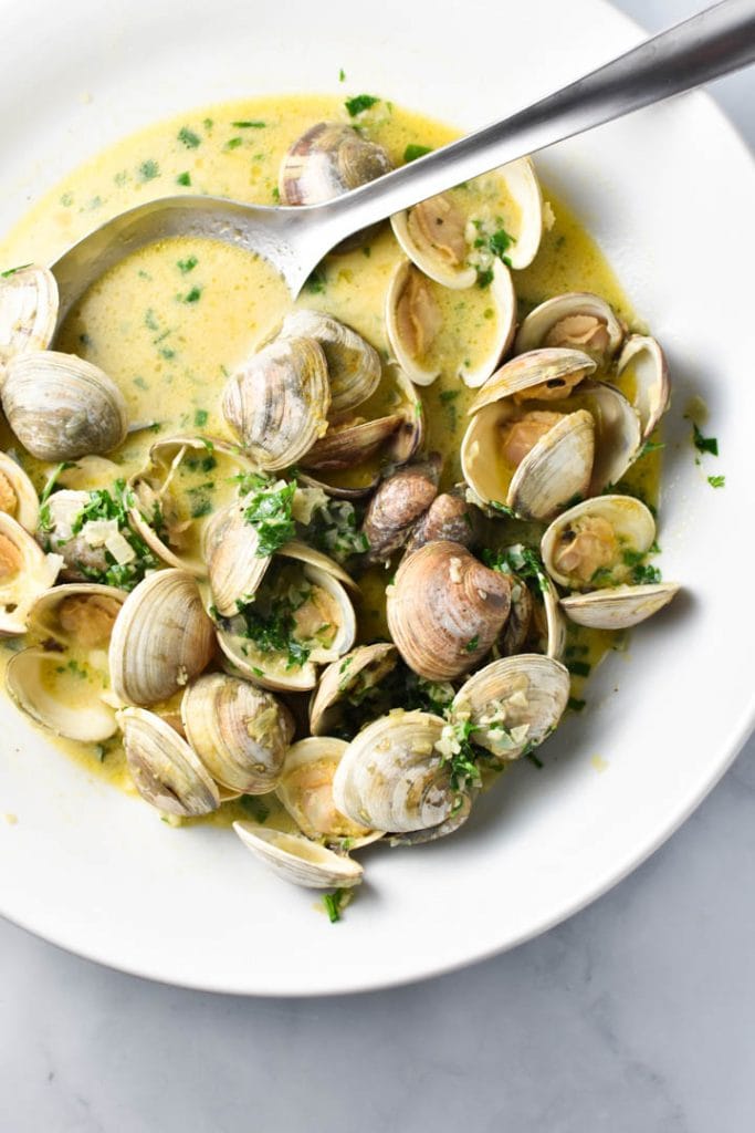 Clams in creamy sauce with parsley in a large white bowl