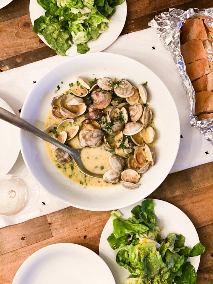 A bowl of clams with two salads and bread on a table