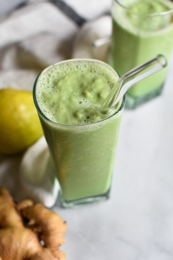 A green pear smoothie on a marble table with ginger and a whole pear