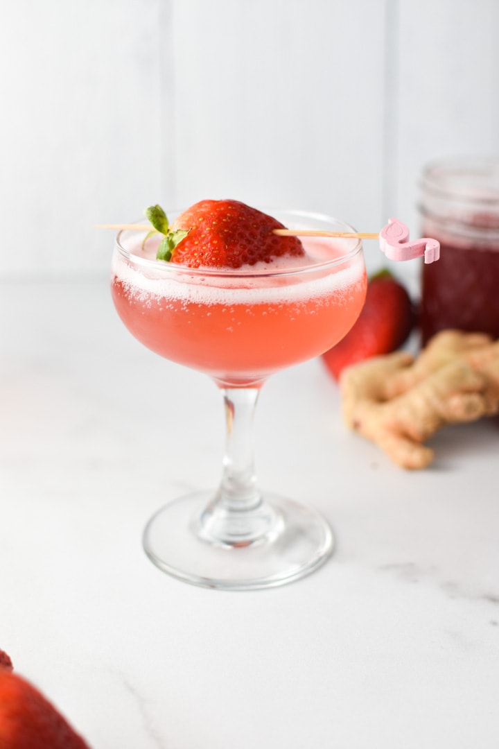 A pink drink fizzing in a coupe glass on a marble surface with a strawberry on top