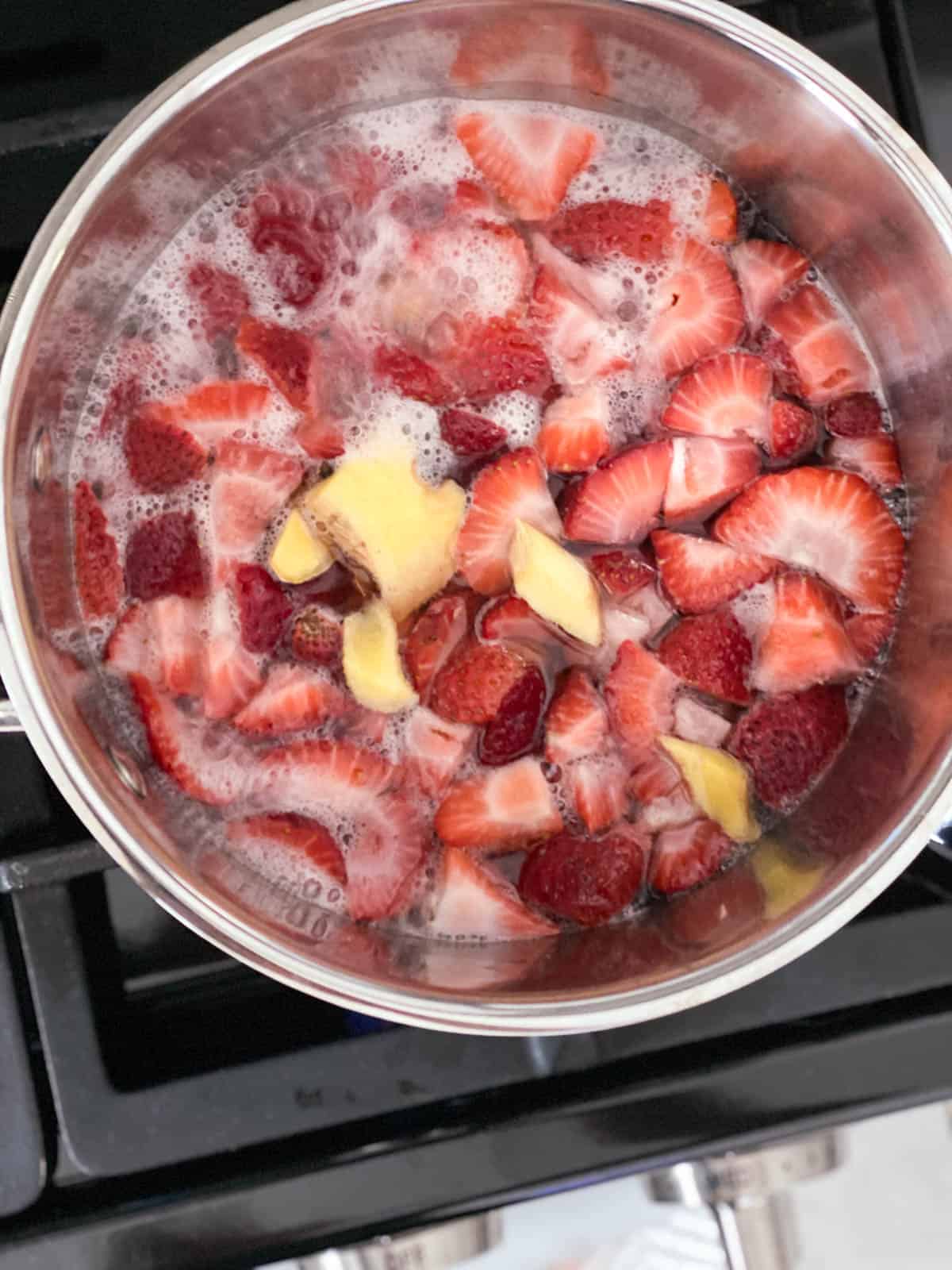Simmering strawberries and ginger in a small pot on the stovetop.