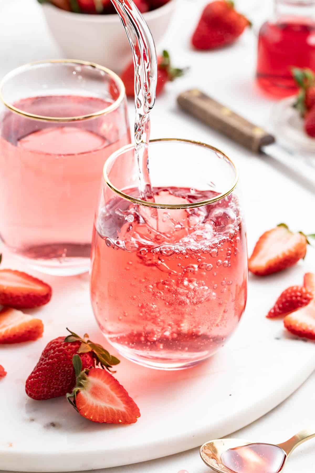 Pouring sparkling water into the strawberry syrup base in a glass with ice.