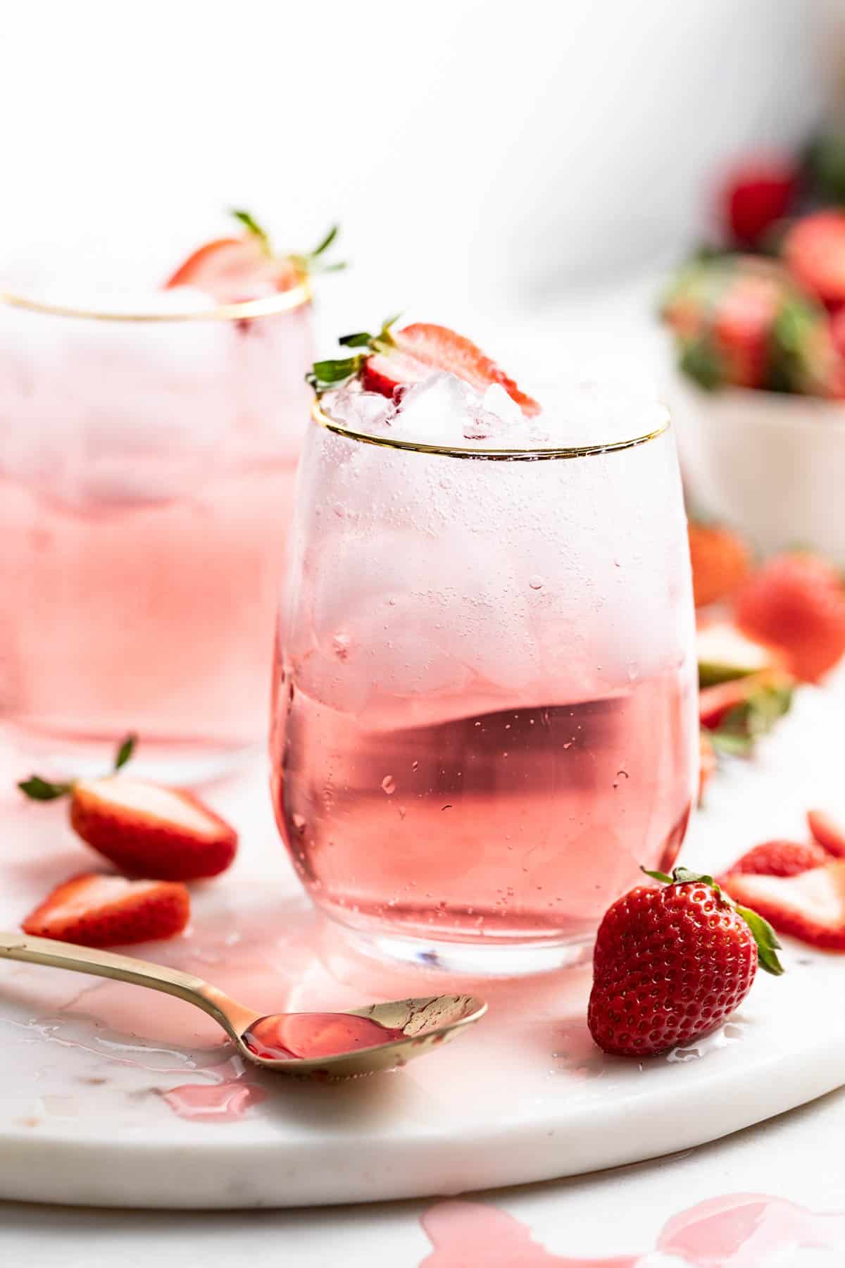 Two strawberry mocktails topped with fresh strawberries and ice. 