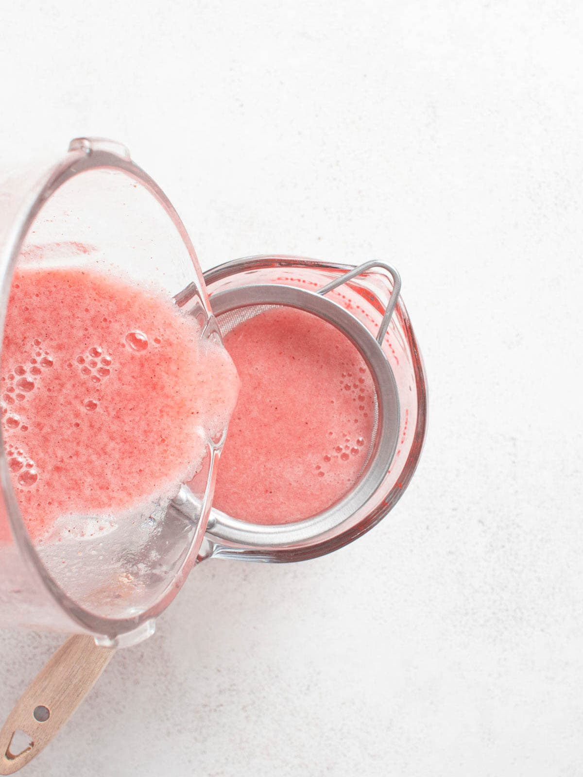 Pouring the strawberry mixture through a fine mesh strainer.