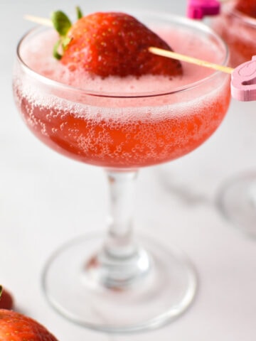 A pink strawberry mocktail spritzer in a coupe glass with a strawberry on the top