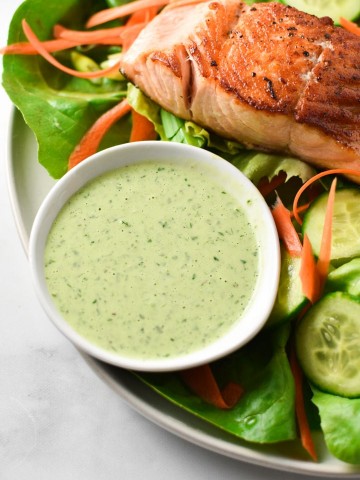 A bowl of creamy basil dressing next to seared salmon on a green salad