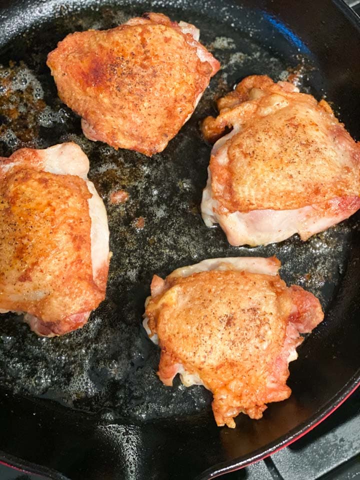 Brown and crispy skin chicken thighs being cooked in a cast iron pan