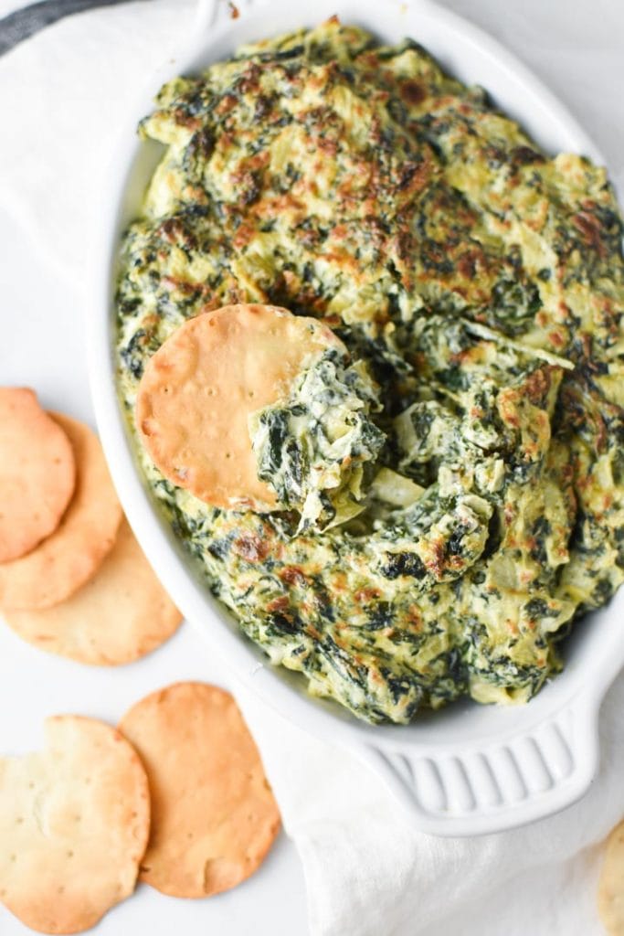 Pita chips topped with creamy spinach artichoke dip on top of a gratin dish filled with dip