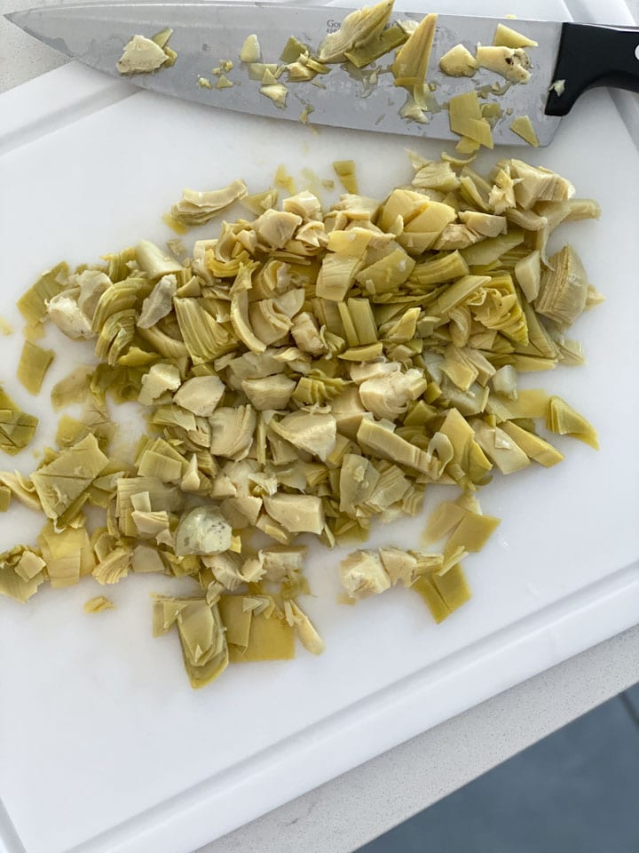 Artichoke hearts being chopped on a white cutting board