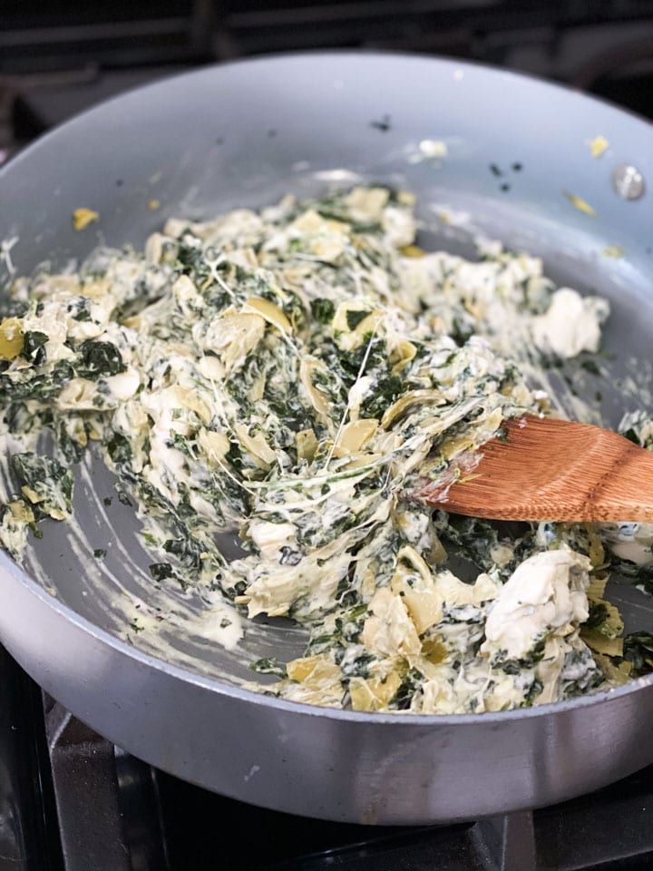 Mixing cheese into the cooked spinach and artichokes in a large pan