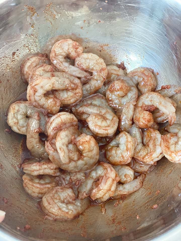 Raw shrimp marinating in a steel bowl.