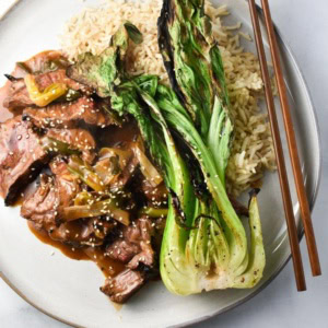 Gluten free mongolian beef with green onions on a plate with grilled bok choy and brown rice