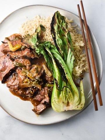 Gluten free mongolian beef with green onions on a plate with grilled bok choy and brown rice