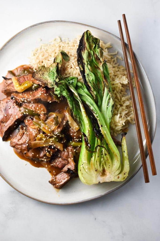 Gluten free mongolian beef with green onions on a plate with grilled bok choy and brown rice