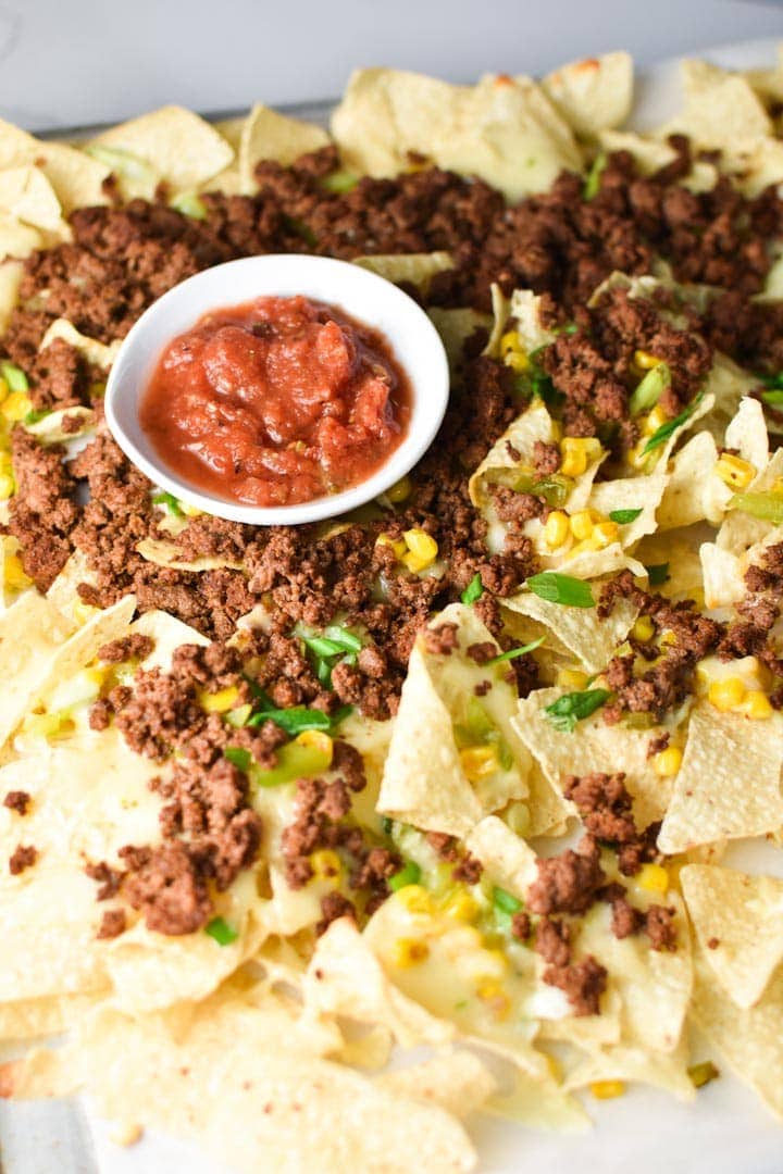 A pile of ground beef nachos with salsa and green onions