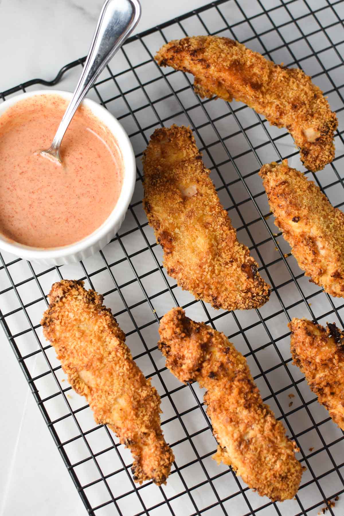 Golden brown tenders on a baking rack next to a honey mustard dip.