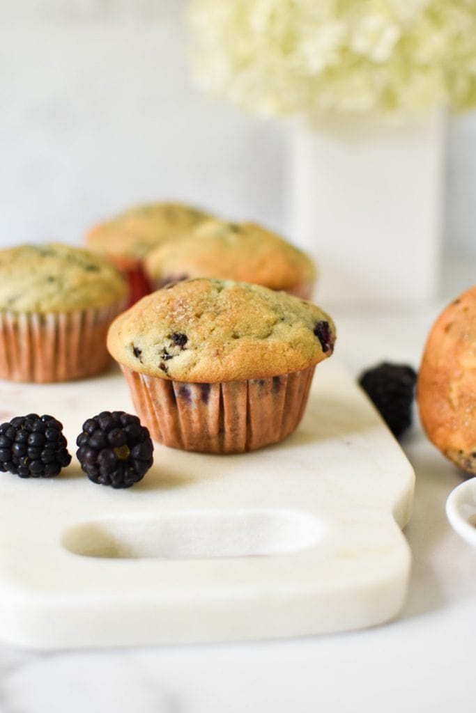 Blackberry muffins on a table with fresh berries and flowers