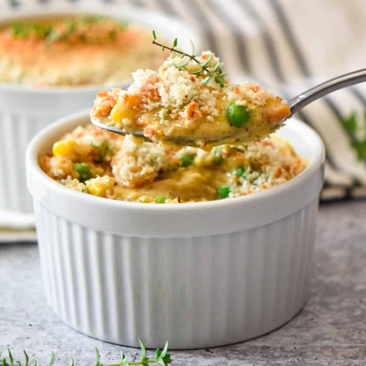 A spoon scooping up chicken pot pie filling from a ramekin dish.