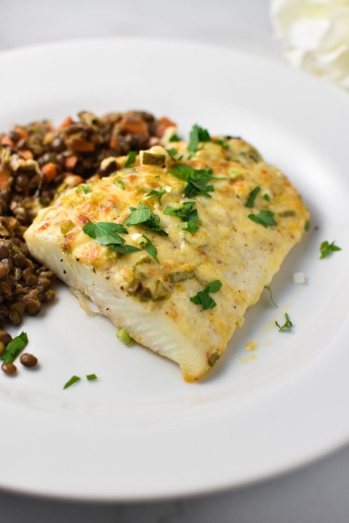 Baked halibut with mayonnaise on a white plate topped with parsley