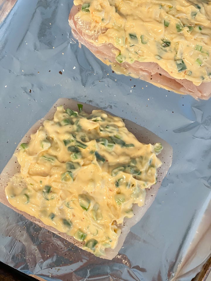 Unbaked halibut filets topped with a mayonnaise sauce on tin foil