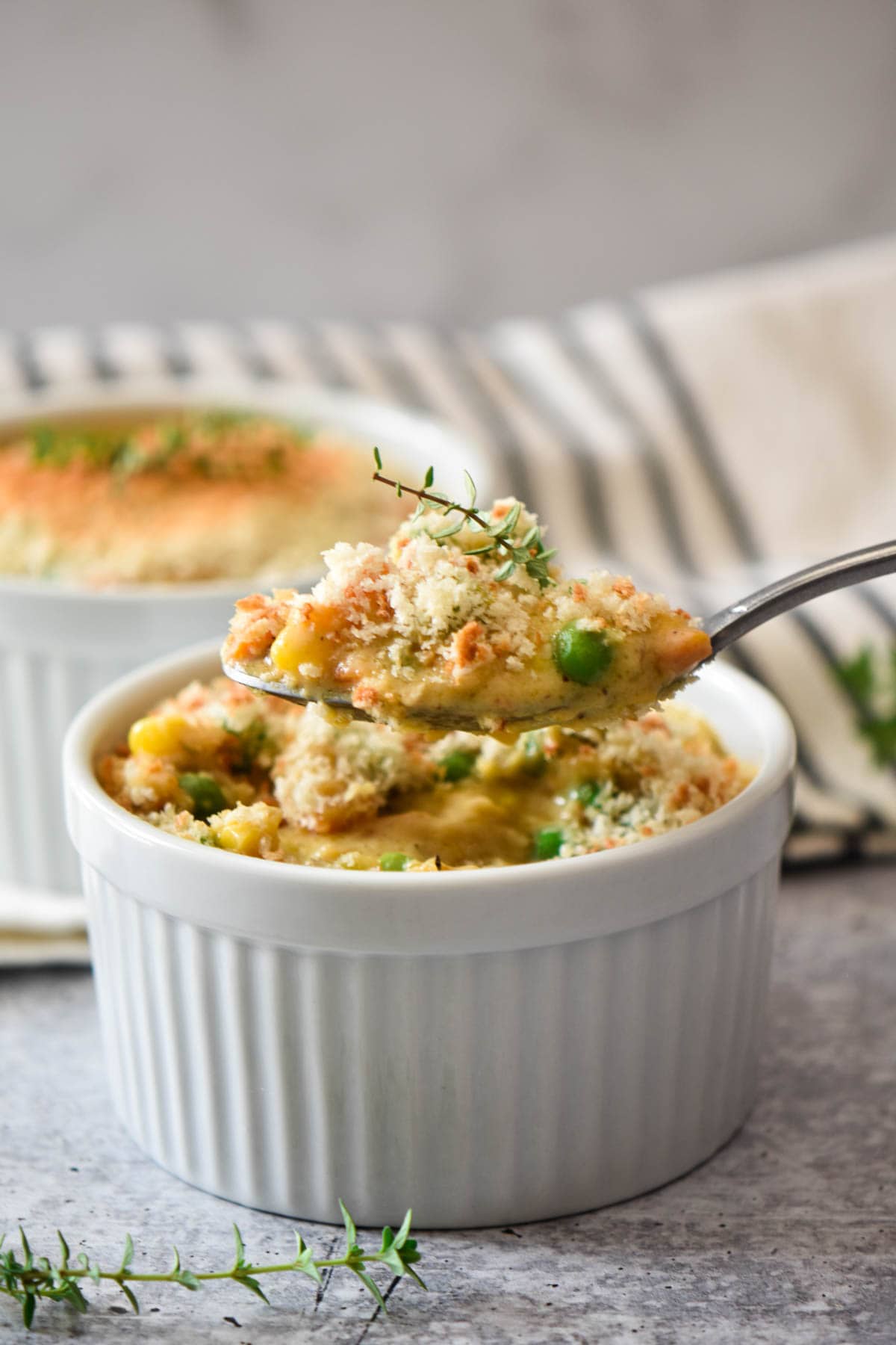 A spoon topped with creamy vegetables and chicken topped with a sprig of fresh thyme