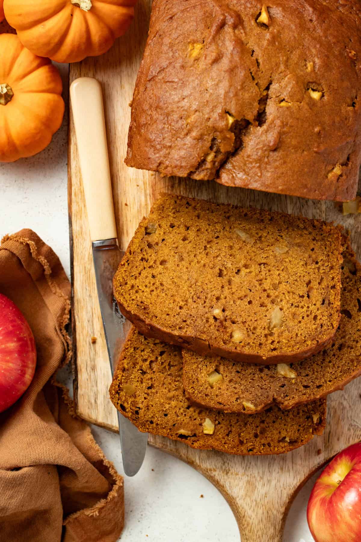 Sliced pumpkin bread with apples on a wood cutting board. 