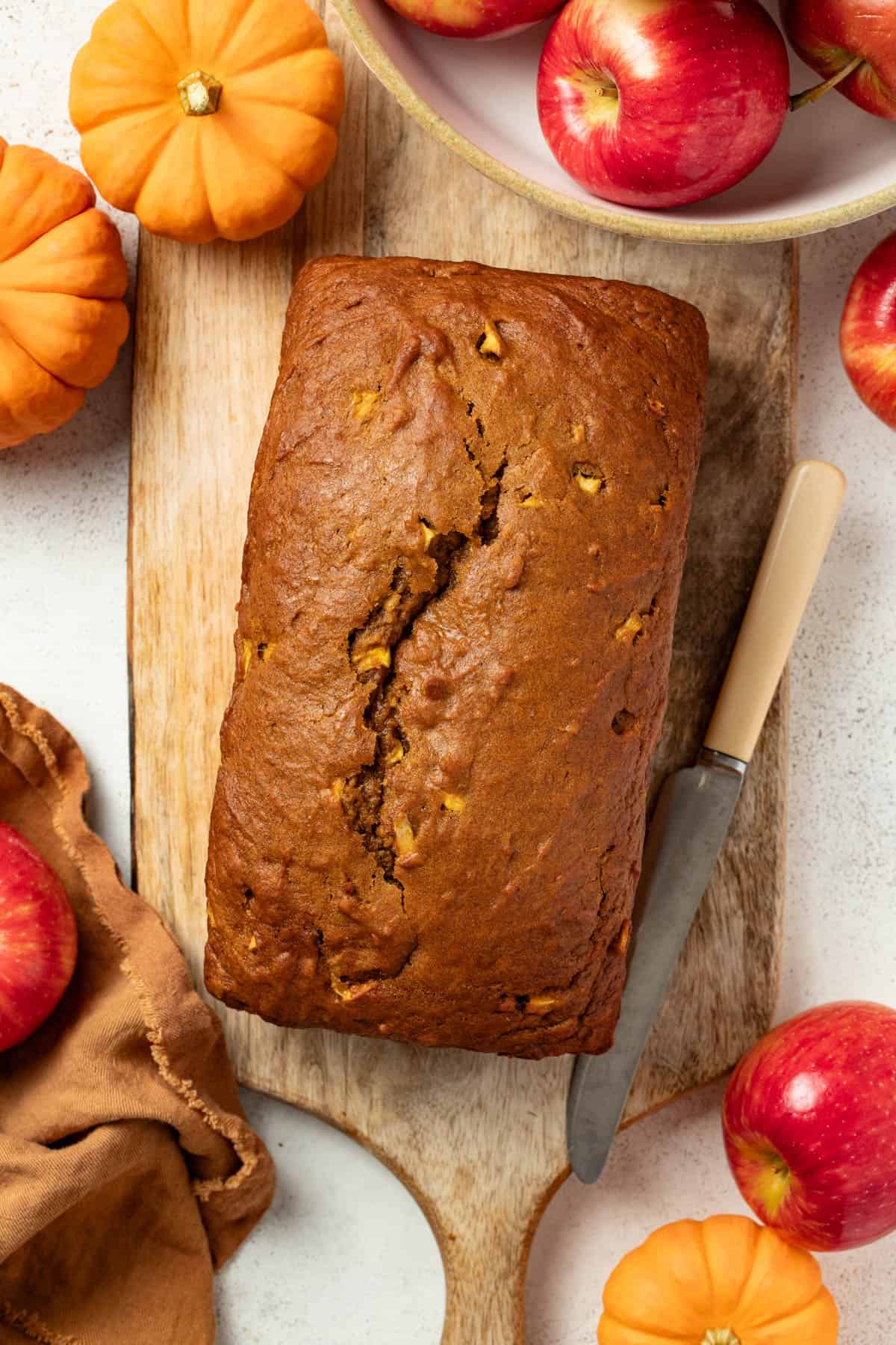 A whole loaf of pumpkin apple bread being cooled on a wood cutting board.