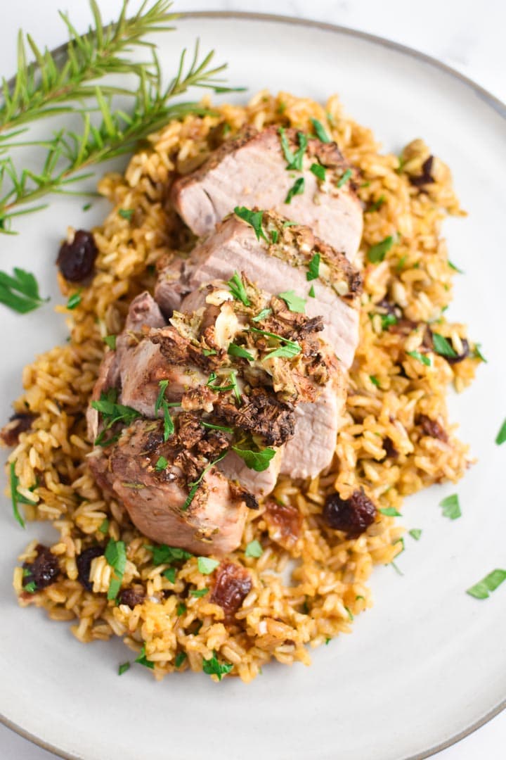 Sliced garlic and rosemary pork tenderloin on rice with rosemary in the background