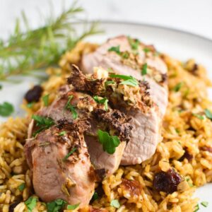 A dijon and rosemary crusted pork tenderloin on top of a rice pilaf with rosemary leaves