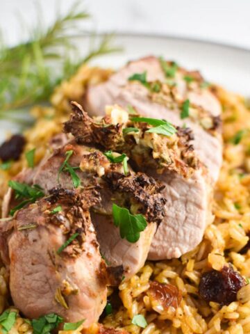 A dijon and rosemary crusted pork tenderloin on top of a rice pilaf with rosemary leaves