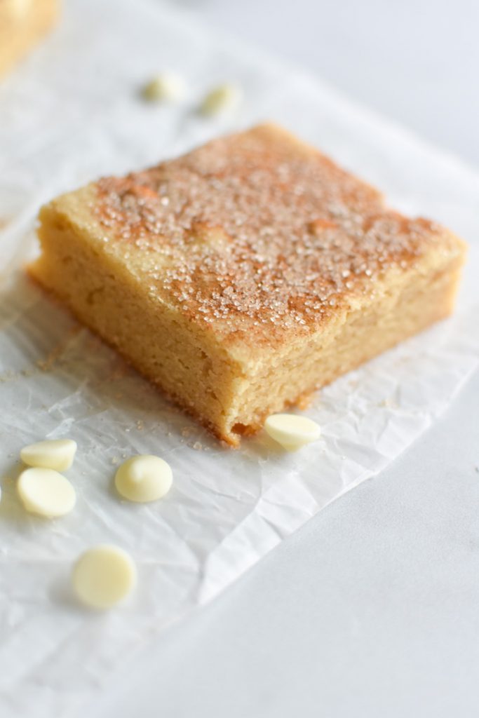 A snickerdoodle blondie on parchment with white chocolate pieces