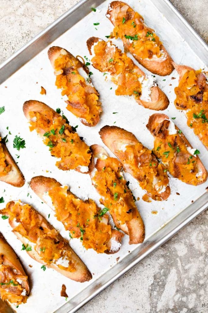 Butternut squash crostini lined up on a sheet pan and sprinkled with mint