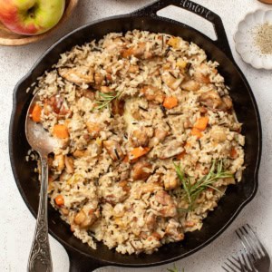 A chicken and wild rice skillet with fresh herbs and vegetables on a white table.